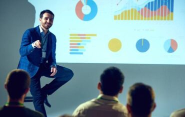 Professional trainer giving talk on data science with detailed analytical visualization projected behind him at a training room.